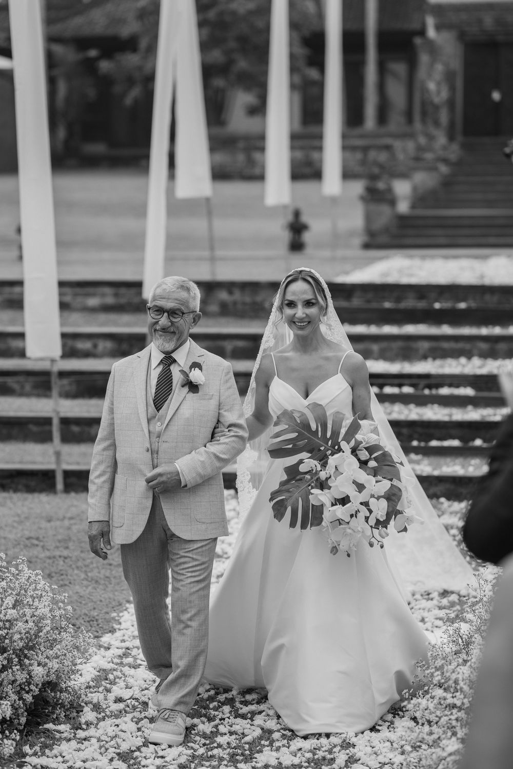 Black and white photo of a bride with her bouquet walking down garden steps.
