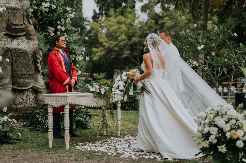Elegant wedding ceremony setup with white floral arrangements and stone statues in a garden setting.