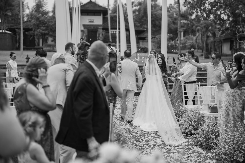 Black and white photo of an outdoor wedding ceremony with guests seated in a garden setting.