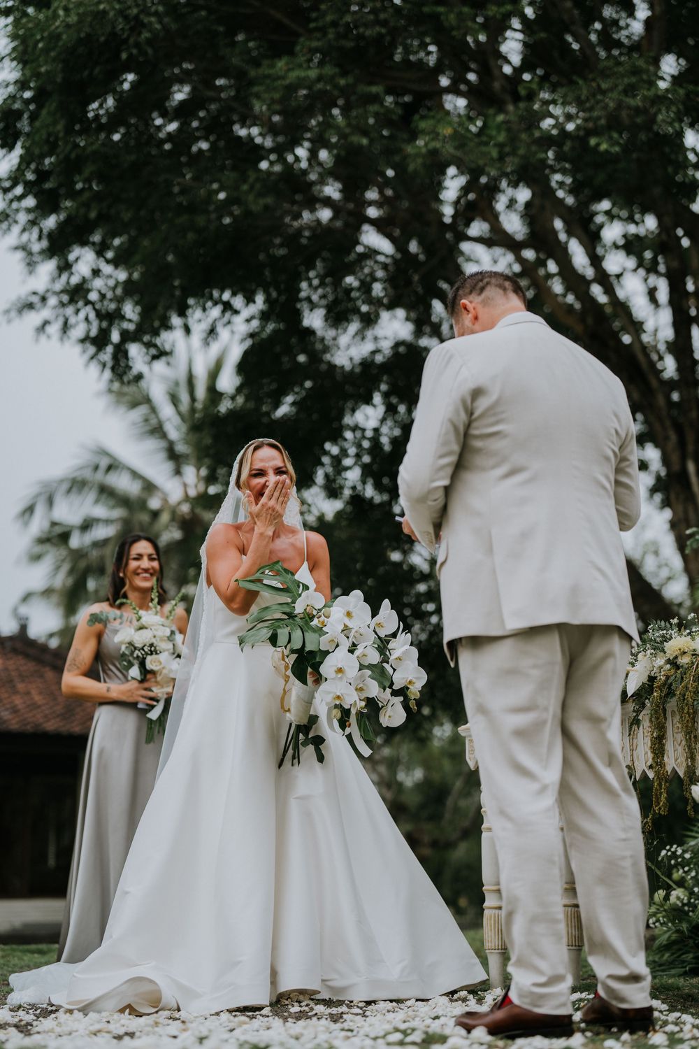 Wedding party in white and cream attire standing together with bouquets in an outdoor garden setting.