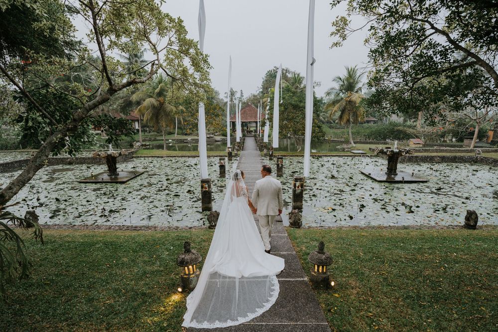 Wedding couple walks down a path lined with white flags in a tropical garden setting.