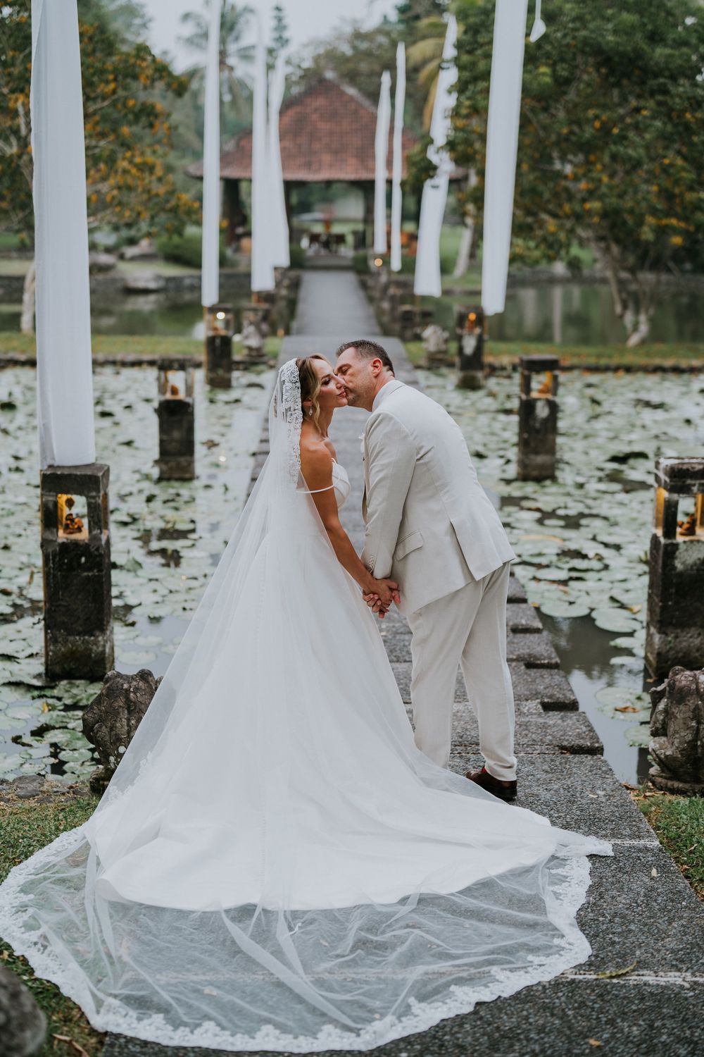 Romantic wedding couple poses among white pillars and candles on a gravel path.