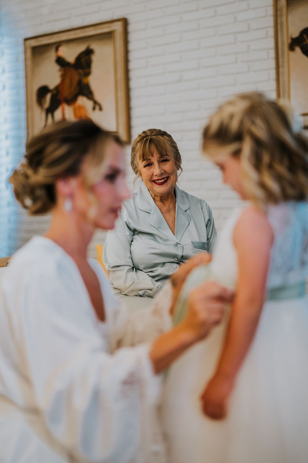 Wedding preparation scene with women in robes sharing a joyful moment in a room with horse artwork.