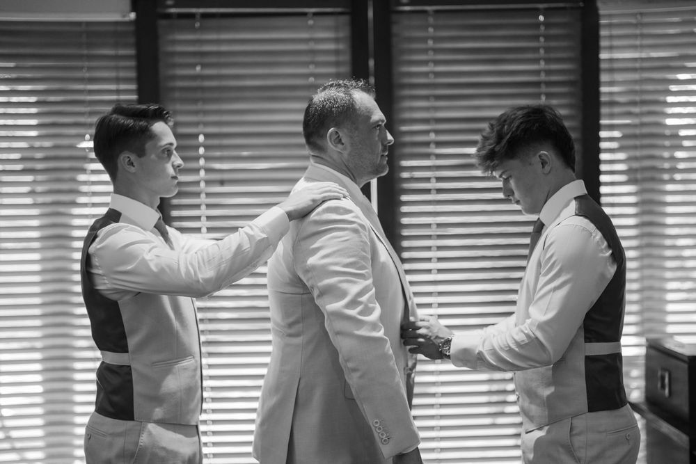Black and white photo of men helping with formal attire preparations.
