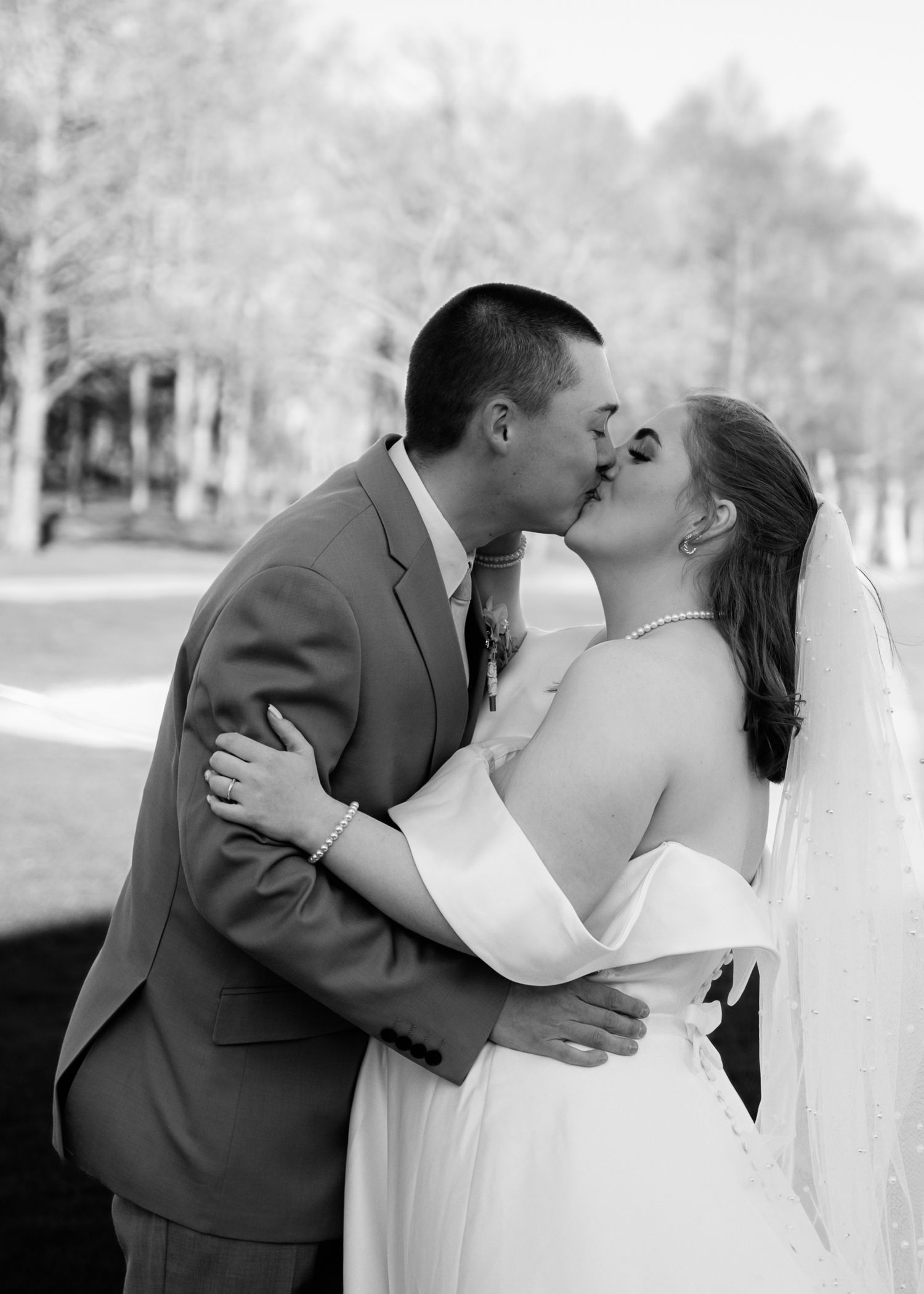A bride and groom share romantic kisses in a series of black and white wedding photographs outdoors.