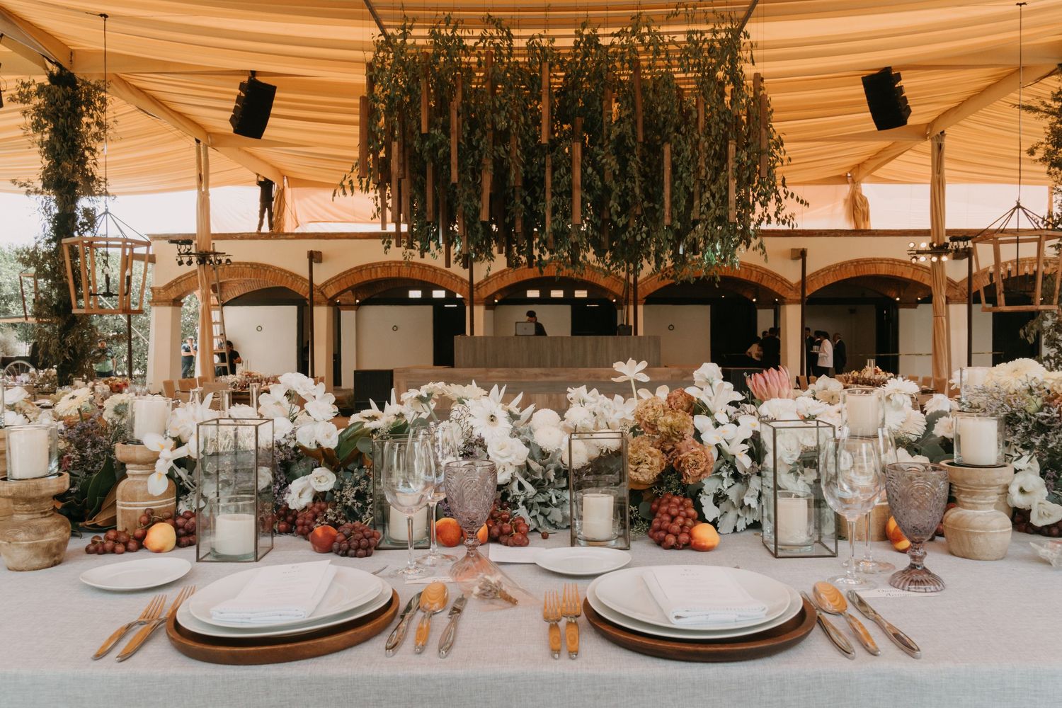 Rustic wedding reception tables decorated with draped fabric, greenery and warm lighting.