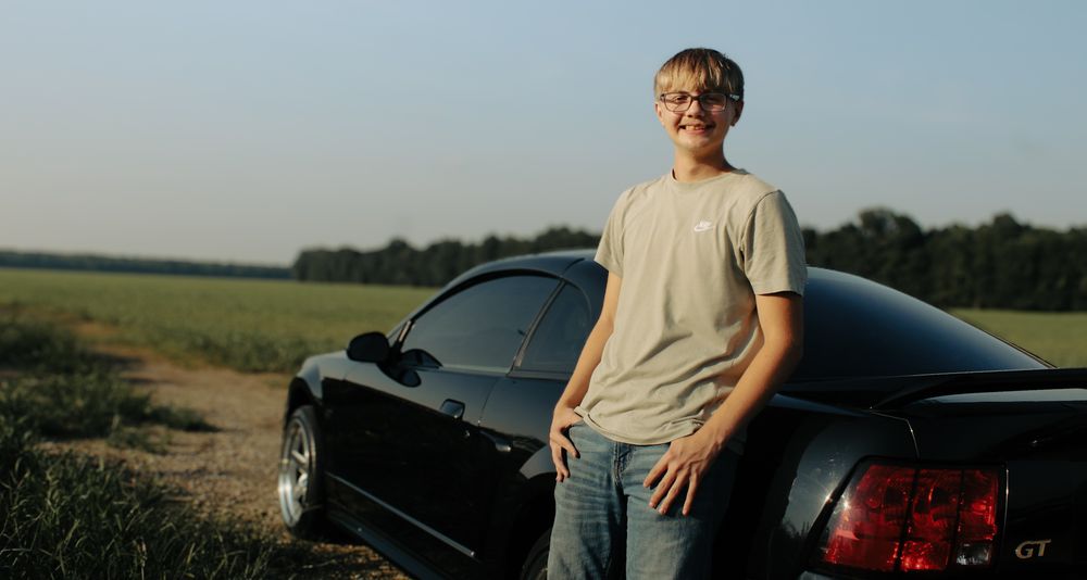 Blayden leaning on his car.
