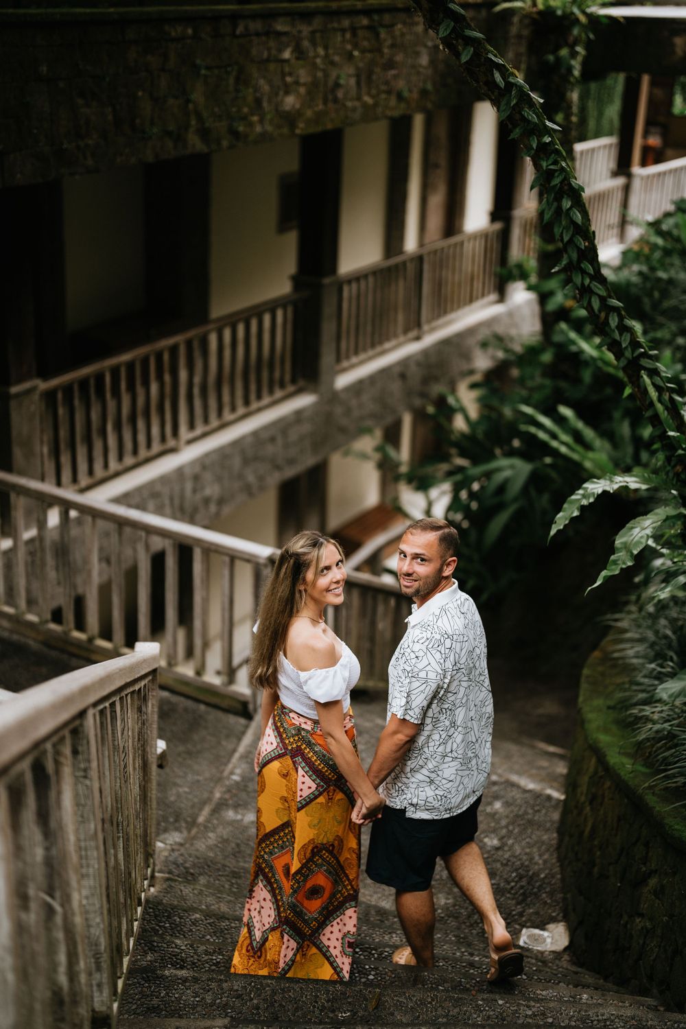 Couple sitting on stone steps surrounded by tropical foliage.