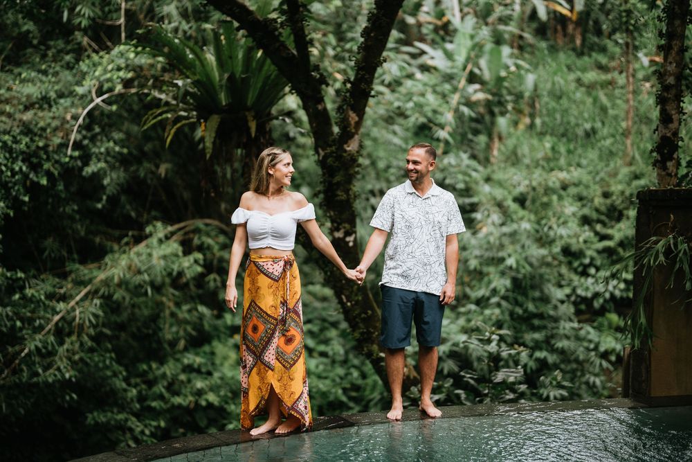 Couples stroll through a scenic garden path with stone walls and tropical vegetation.
