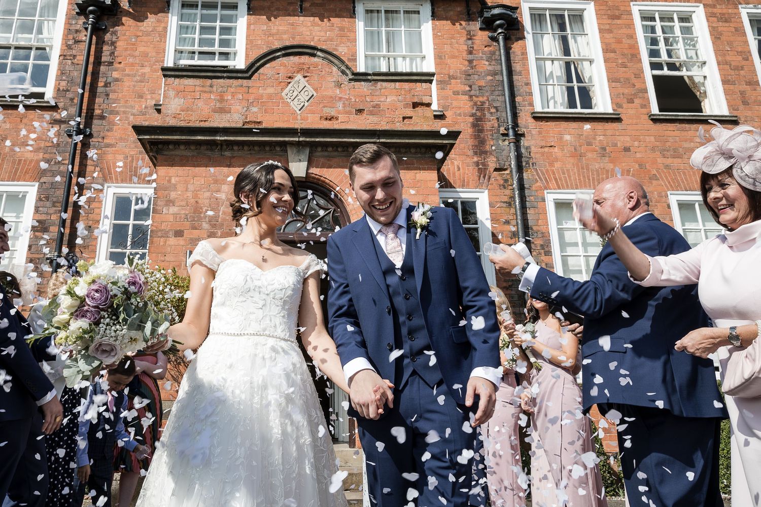 Bride and groom on Kelham House steps surrounded by confetti and cheering guests.
