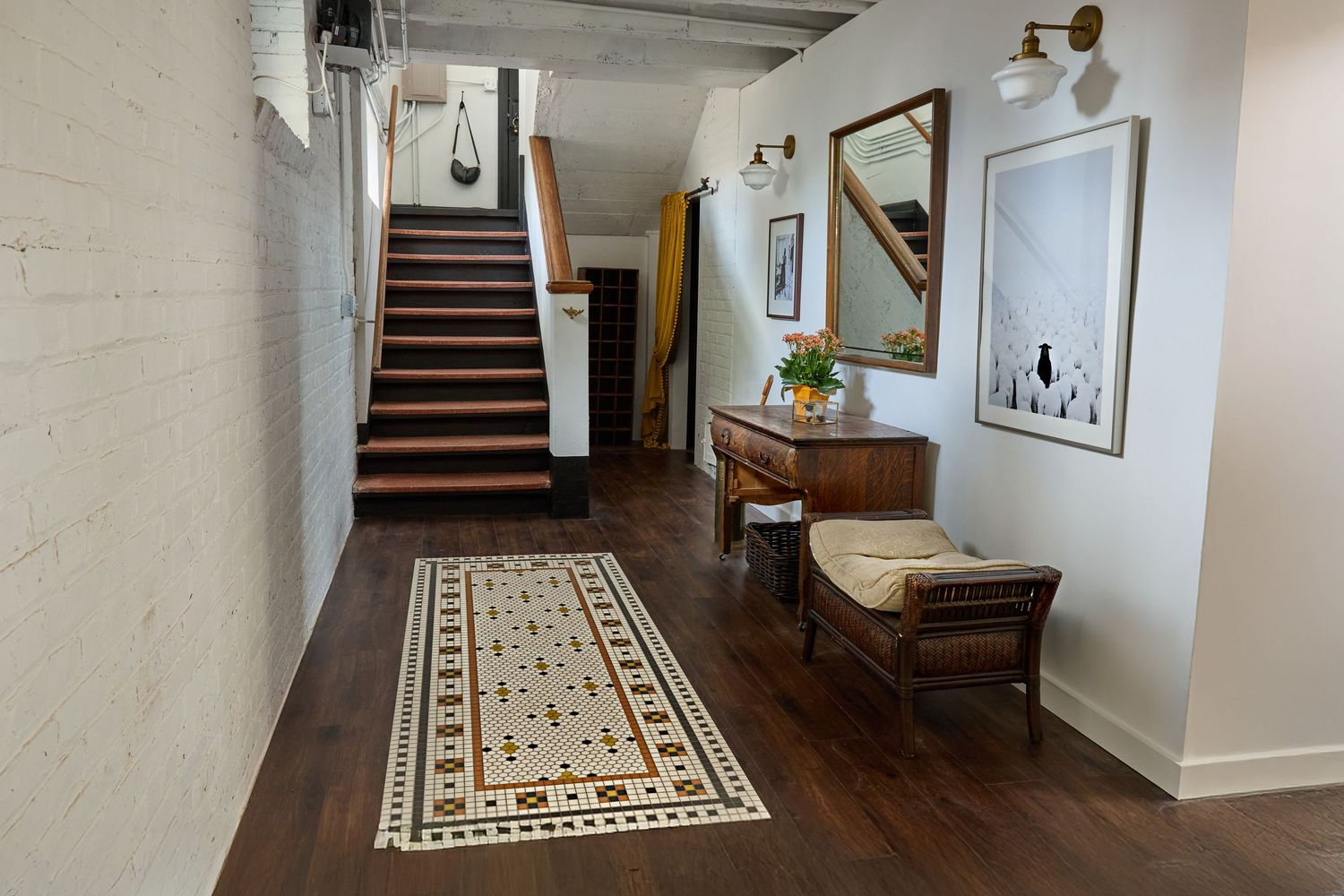 Modern basement hallway with white walls, patterned area rug, and wall-mounted lighting fixtures.