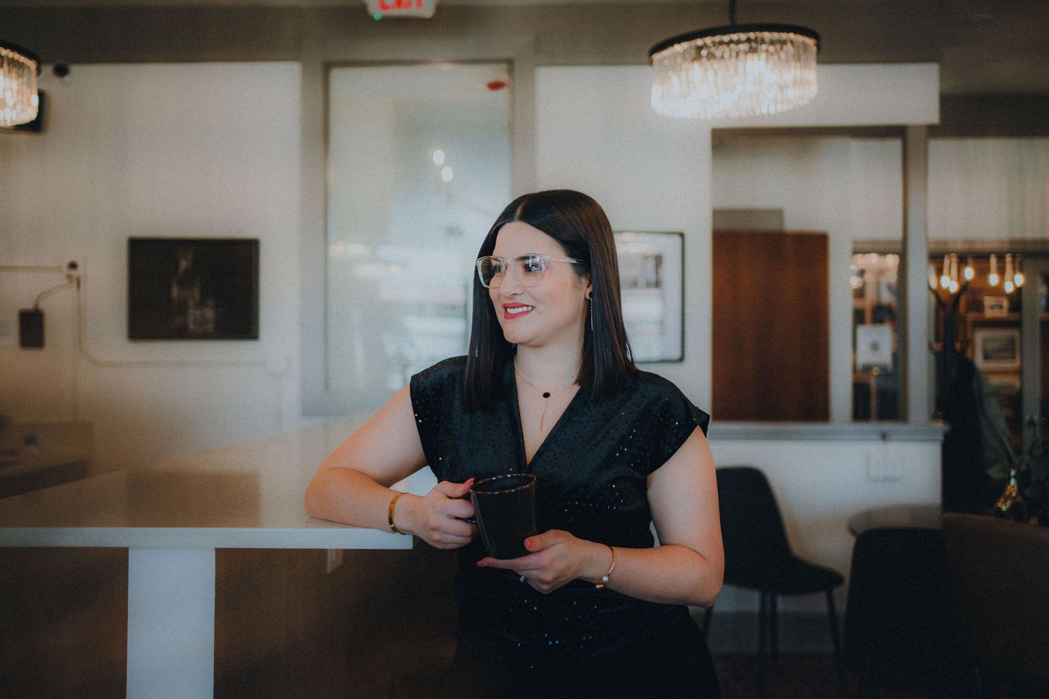 Server in black uniform standing at bar counter in modern restaurant interior.