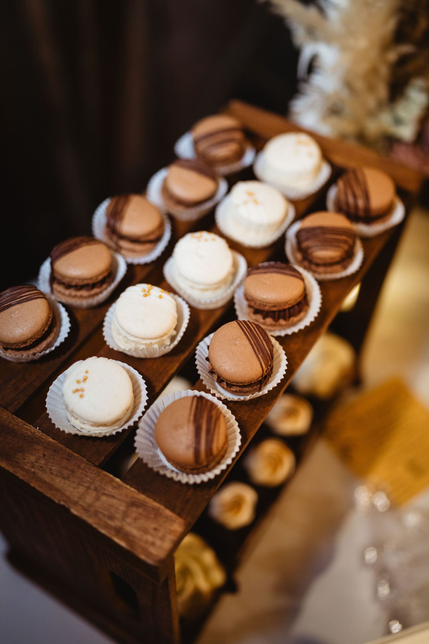 Brown and white macarons arranged in rows on a rustic wooden display tray at a dessert table.