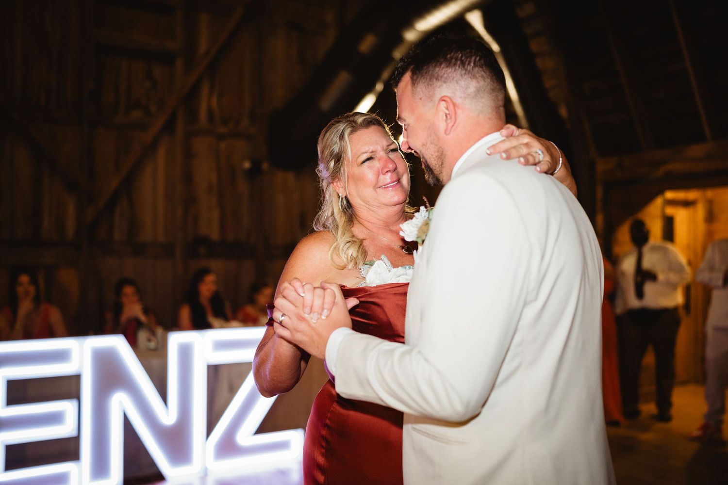 A couple shares a romantic dance together in a dimly lit rustic barn venue during a wedding celebration.