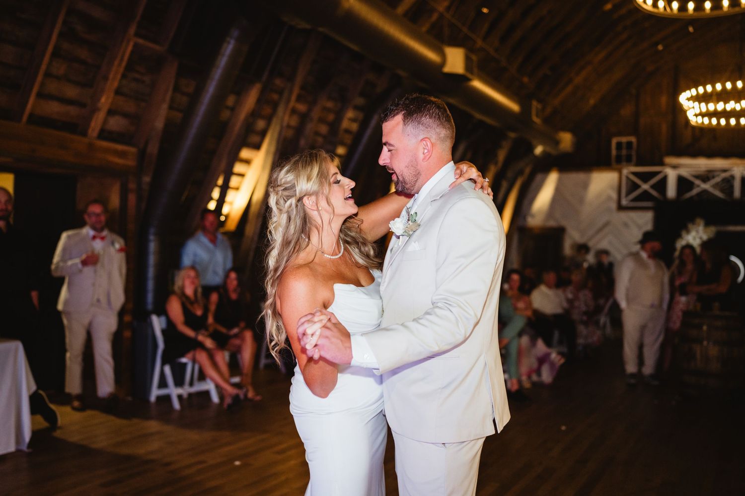 Couples dancing together in an elegantly lit rustic barn venue during an evening celebration.