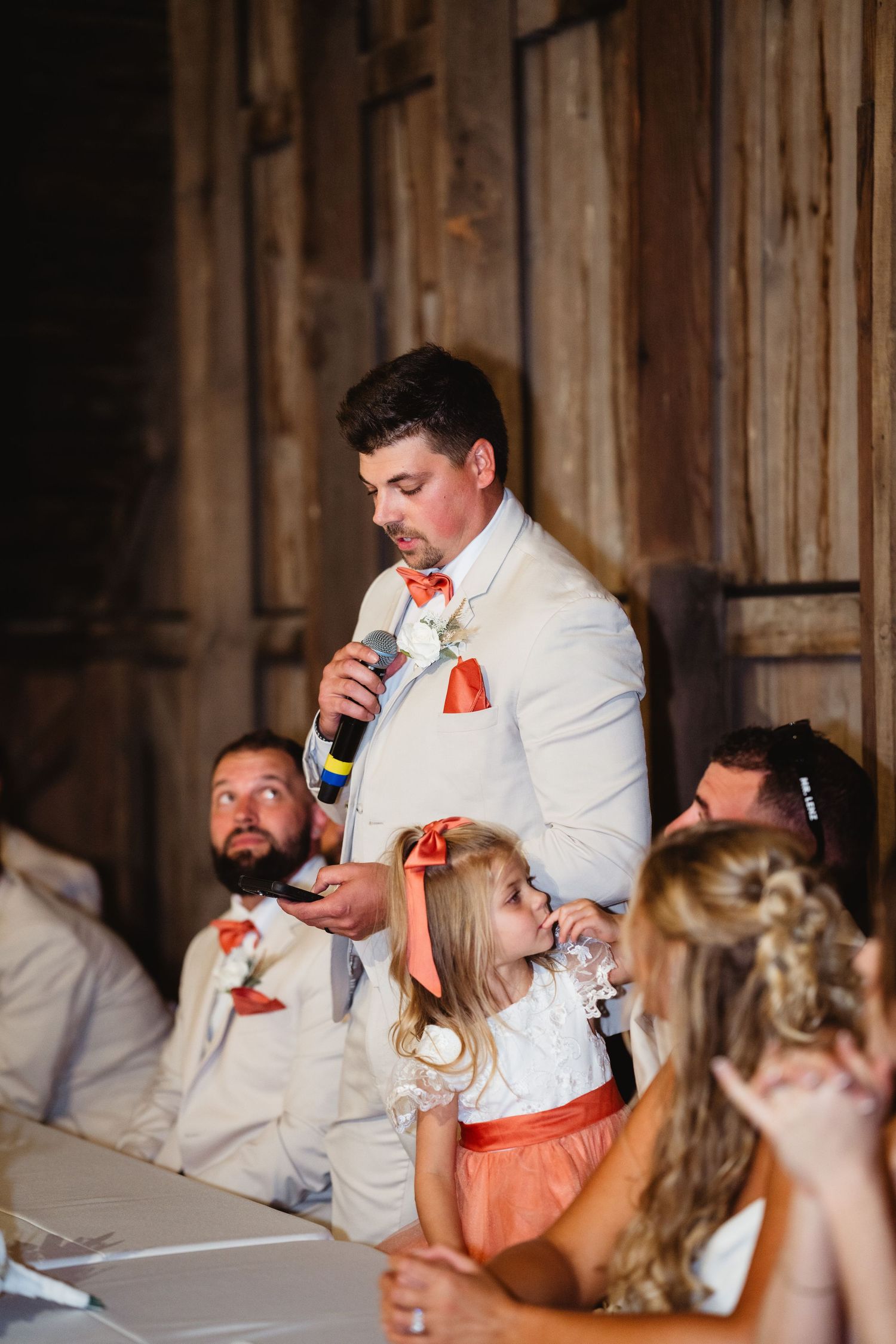 Wedding reception guests enjoying emotional speeches and reactions in a rustic barn venue.