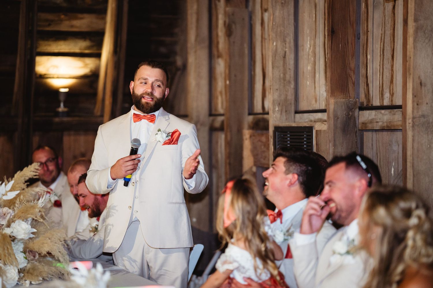 A group enjoying a lively moment of celebration and laughter inside a rustic wooden barn reception venue.