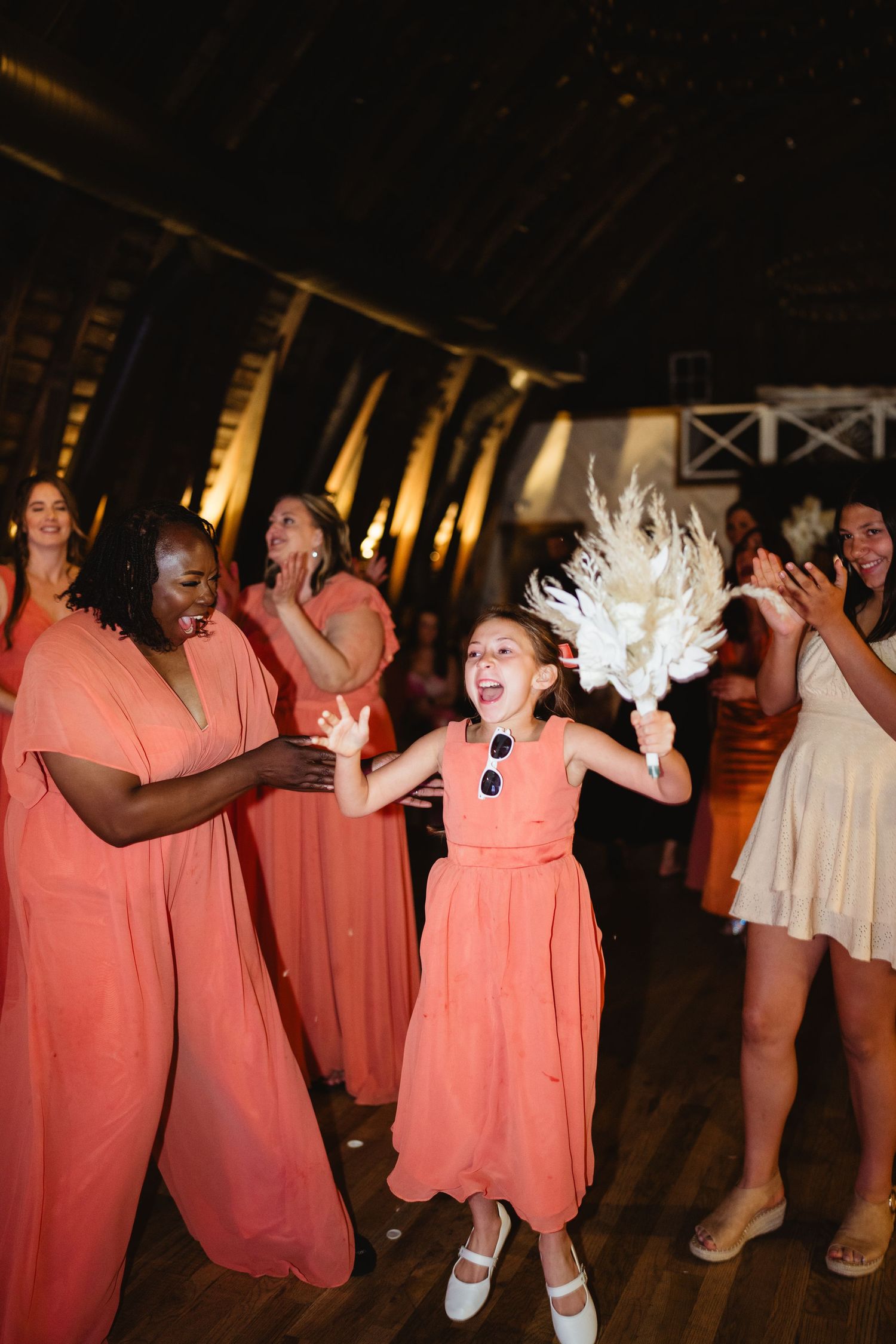 A group of people in coral-colored dresses dancing enthusiastically at a wedding reception party.