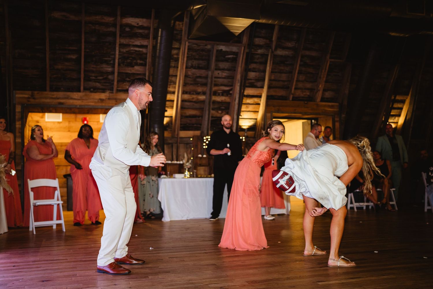 A wedding party performs a fun choreographed dance routine together on the dance floor in a rustic barn venue.