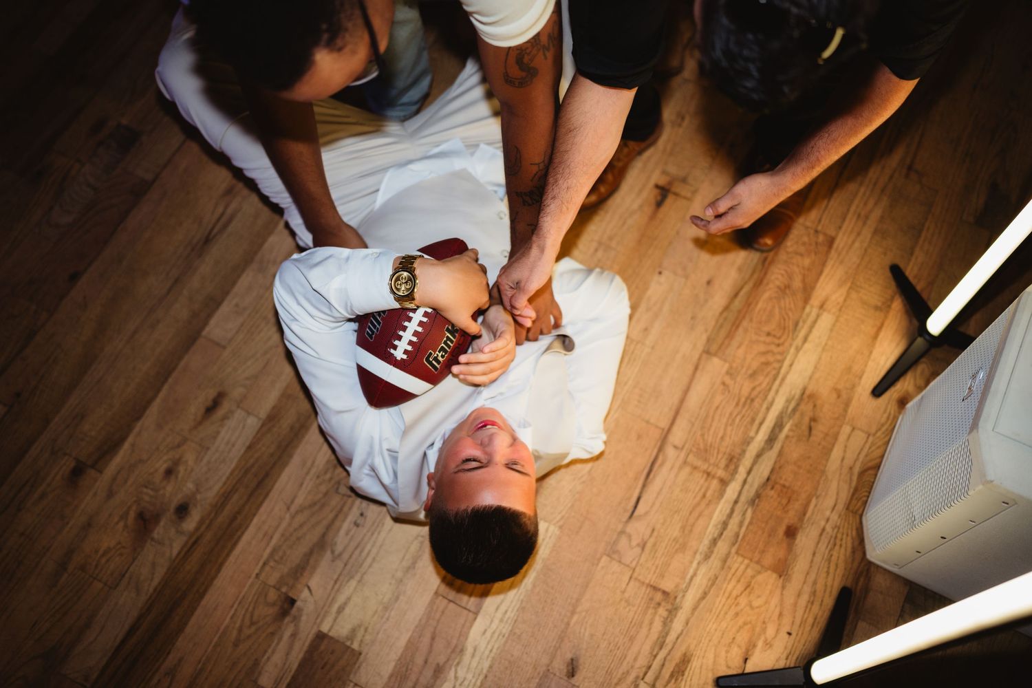 High impact play sequence of collegiate or high school football players diving for a ball on a hardwood floor.