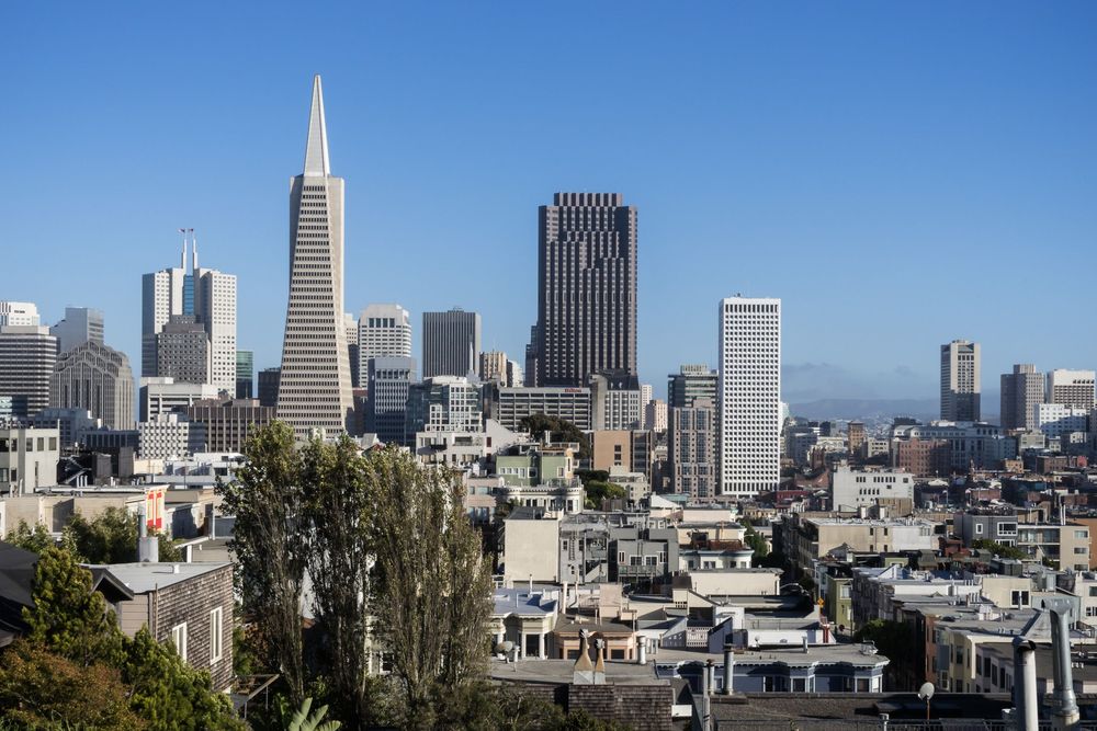Panoramic view of San Francisco skyline featuring iconic Transamerica Pyramid and downtown buildings against blue sky.
