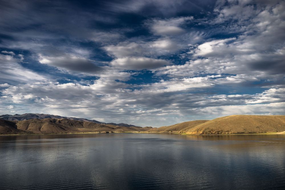 A scenic mountain lake in a barren landscape with dramatic clouds and reflective water under stormy skies.