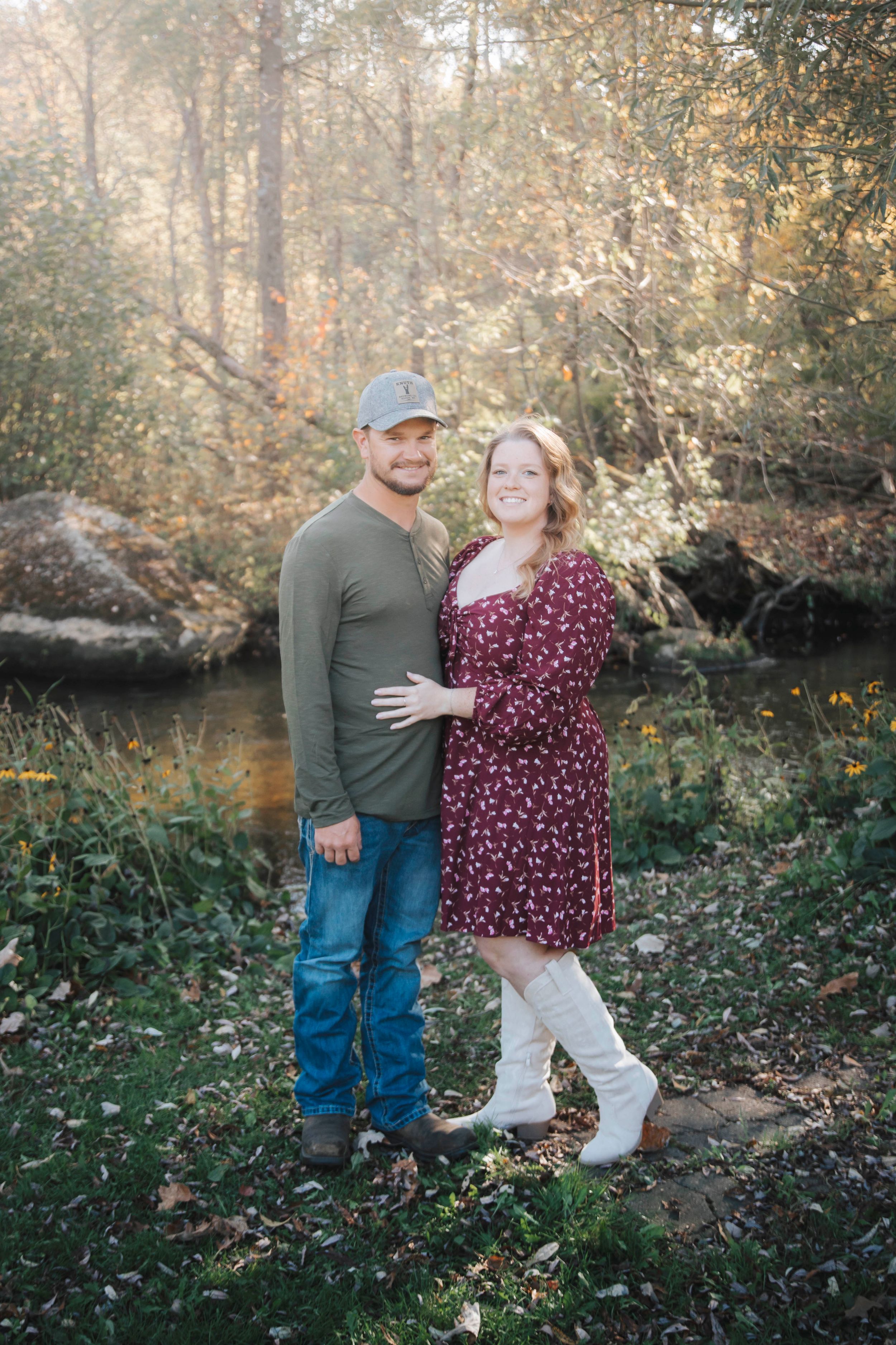 A couple shares a playful moment together by a creek during an autumn outdoor photoshoot.