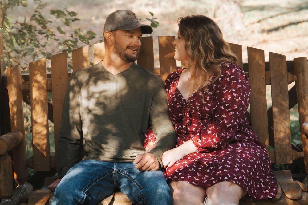A couple sits outdoors sharing an intimate moment together in casual fall attire.