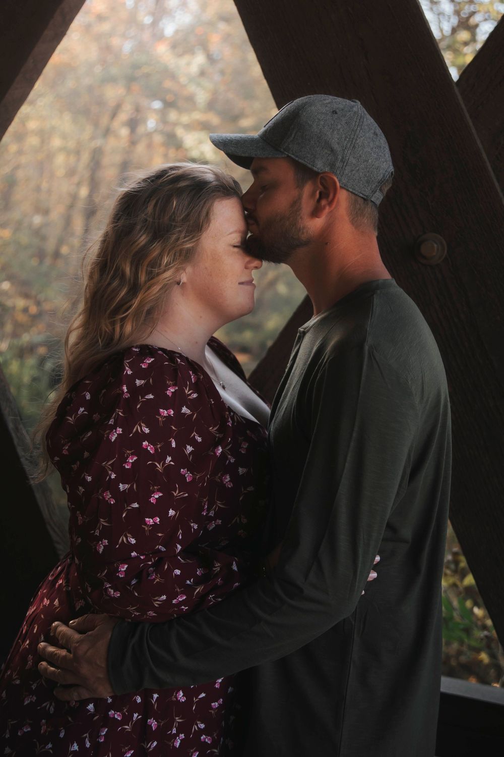 A romantic couple embraces in intimate poses against a dark wooded backdrop during a photo session.