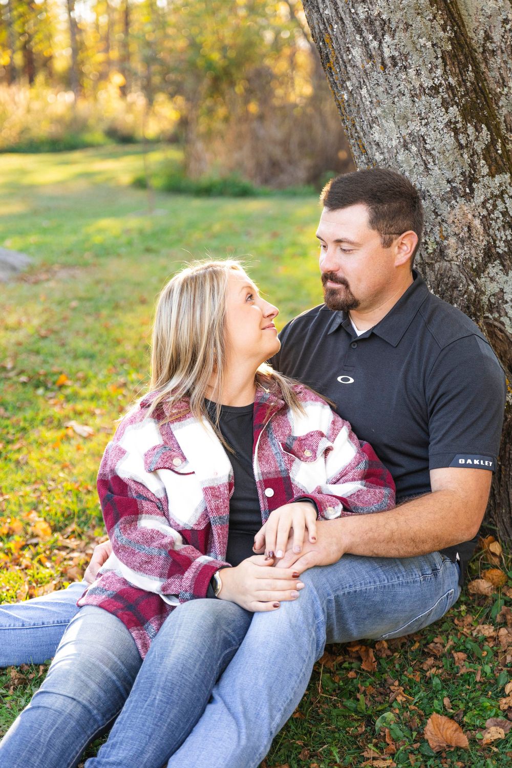 A couple sits together under a tree during autumn, sharing intimate moments in the golden afternoon light.