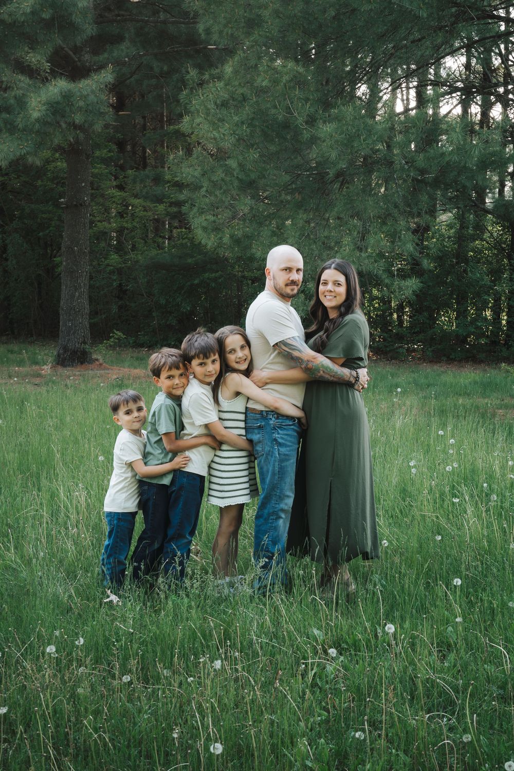 A playful family group huddles together in a grassy field surrounded by pine trees.