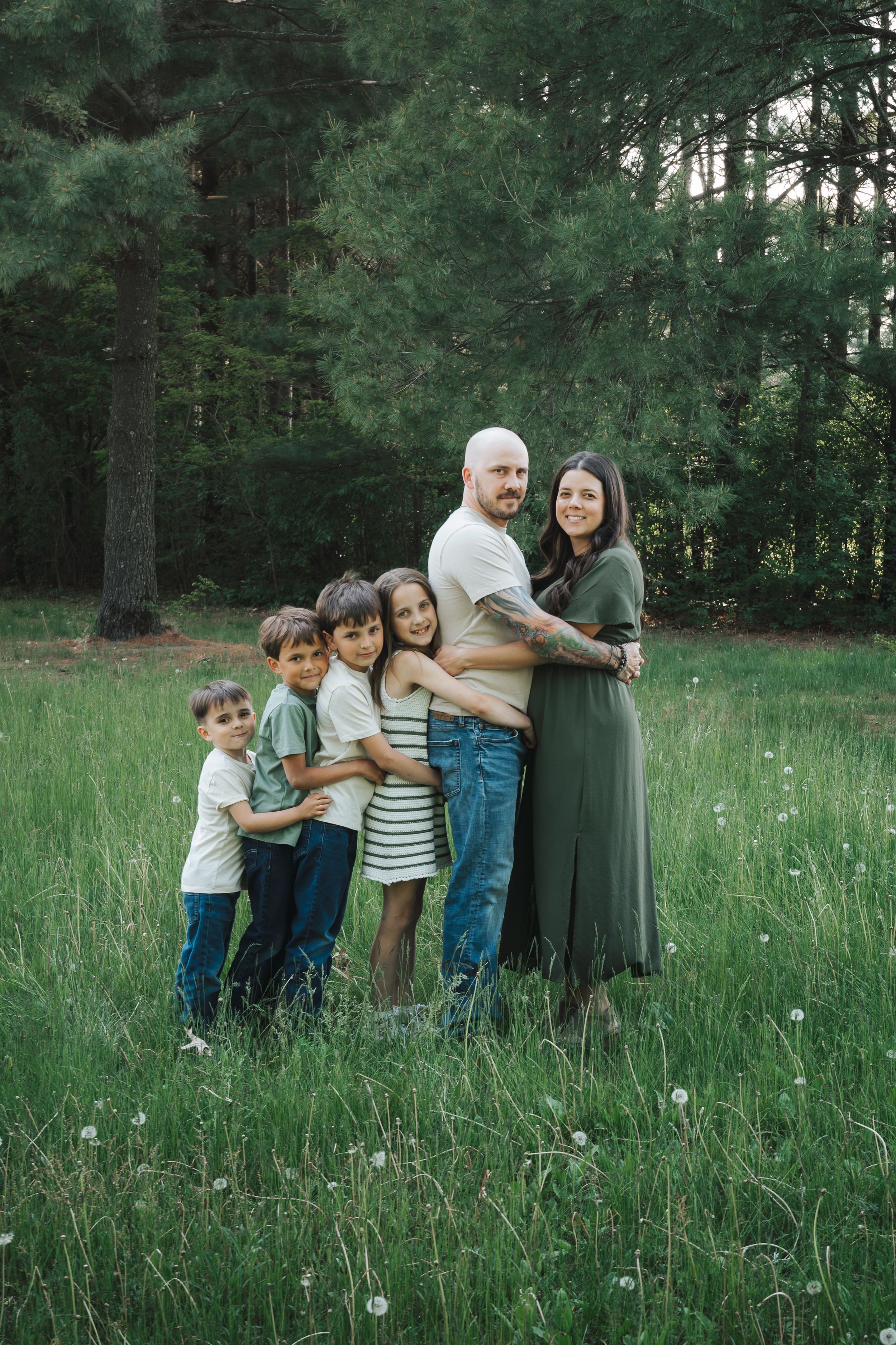 A playful family group huddles together in a grassy field surrounded by pine trees.