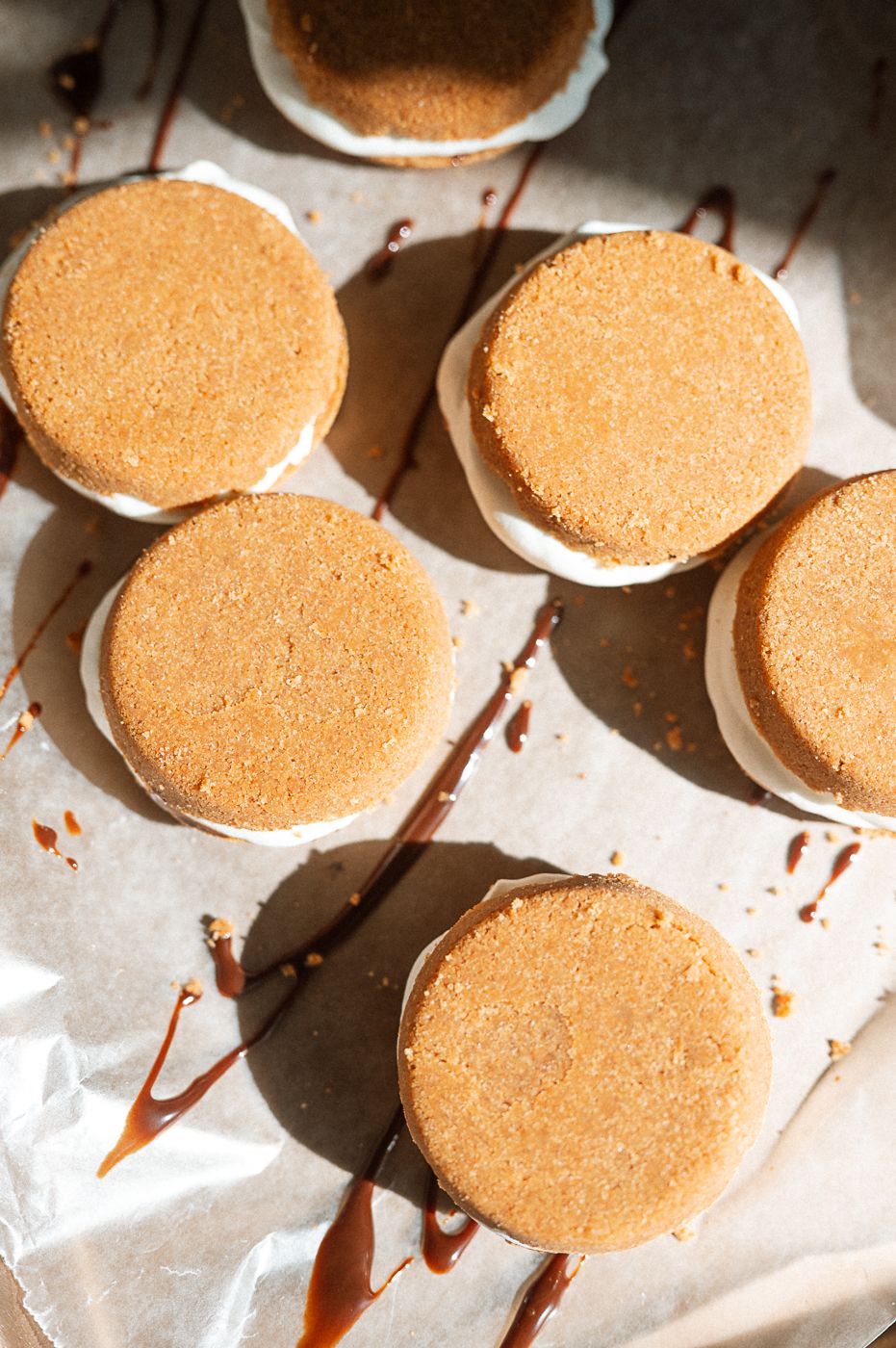 Freshly baked chocolate macarons arranged in rows on white parchment paper with a dark chocolate drizzle.