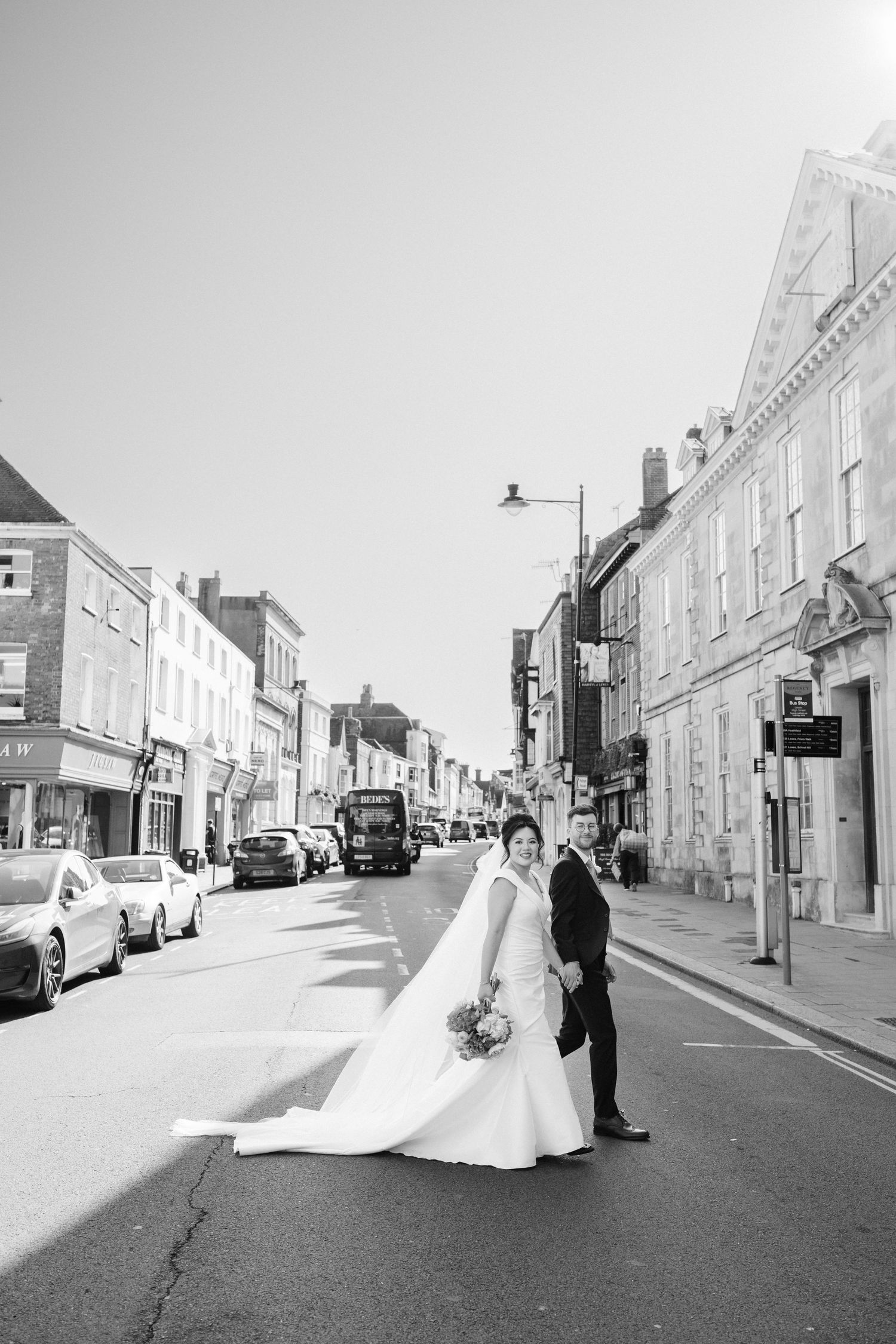 A couple walks down a charming cobblestone street in black and white, creating an elegantly timeless wedding scene.