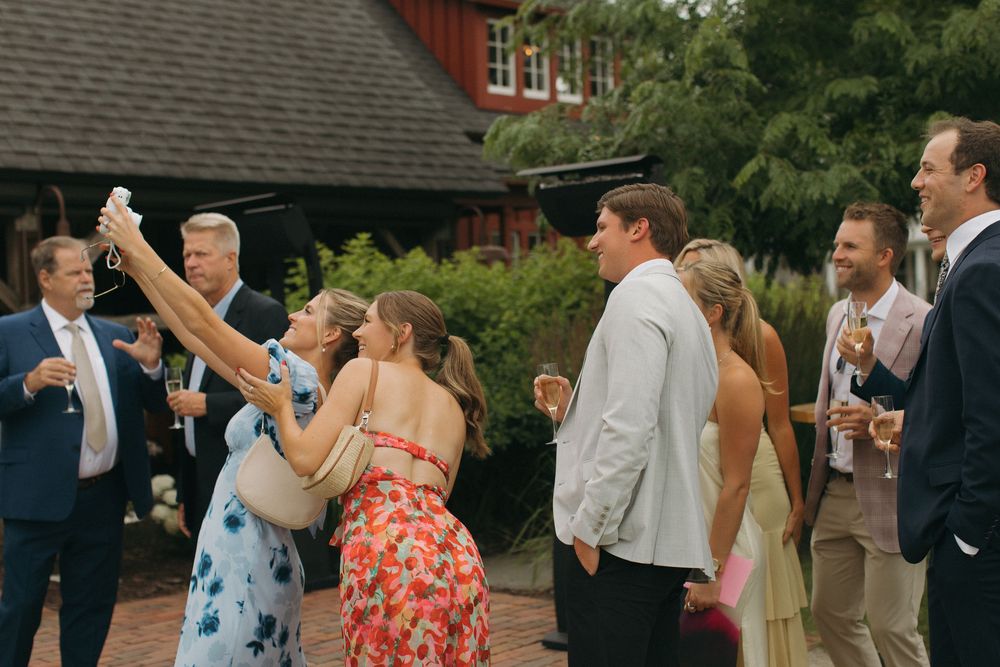 Wedding guests socializing and taking photos at outdoor reception.