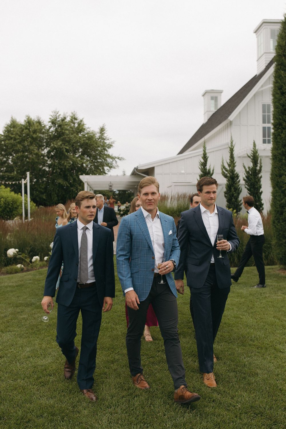 Three men in suits walking across lawn near white building.