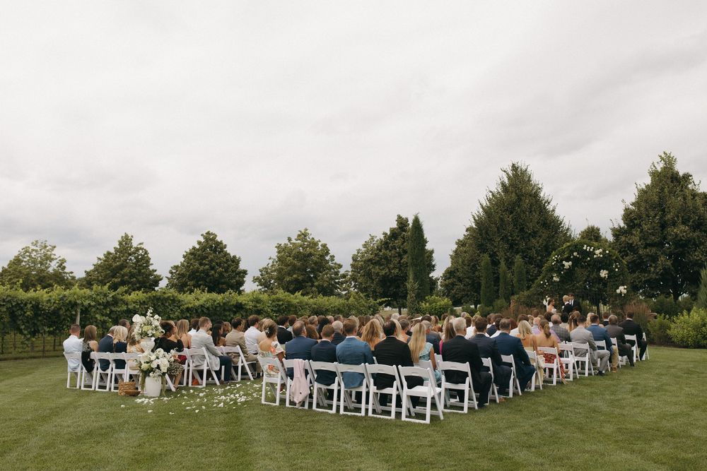 Panoramic view of an outdoor wedding ceremony setup with white chairs on a green lawn.