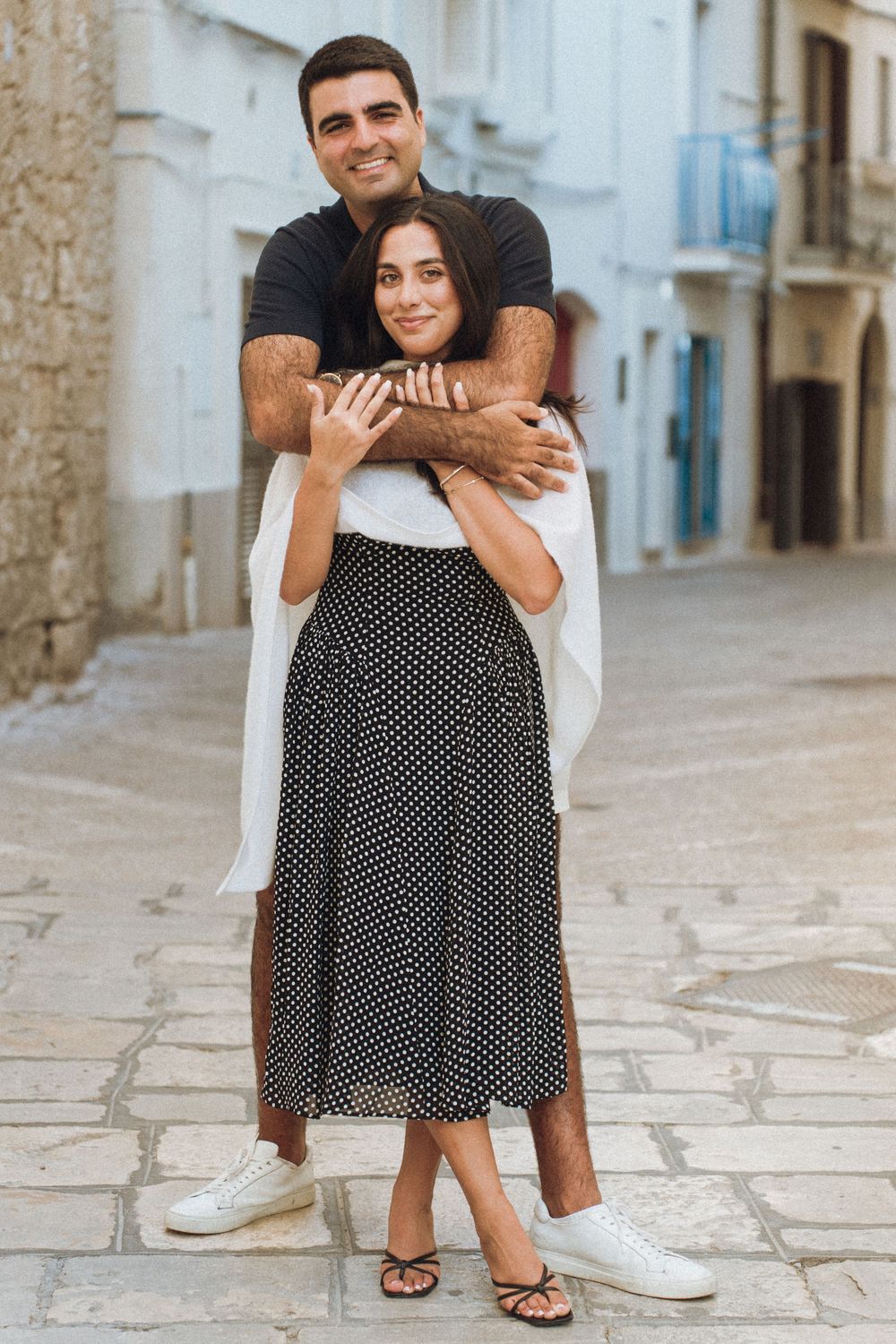 A polka dot dress and white sneakers visible in a romantic photoshoot along cobblestone streets.