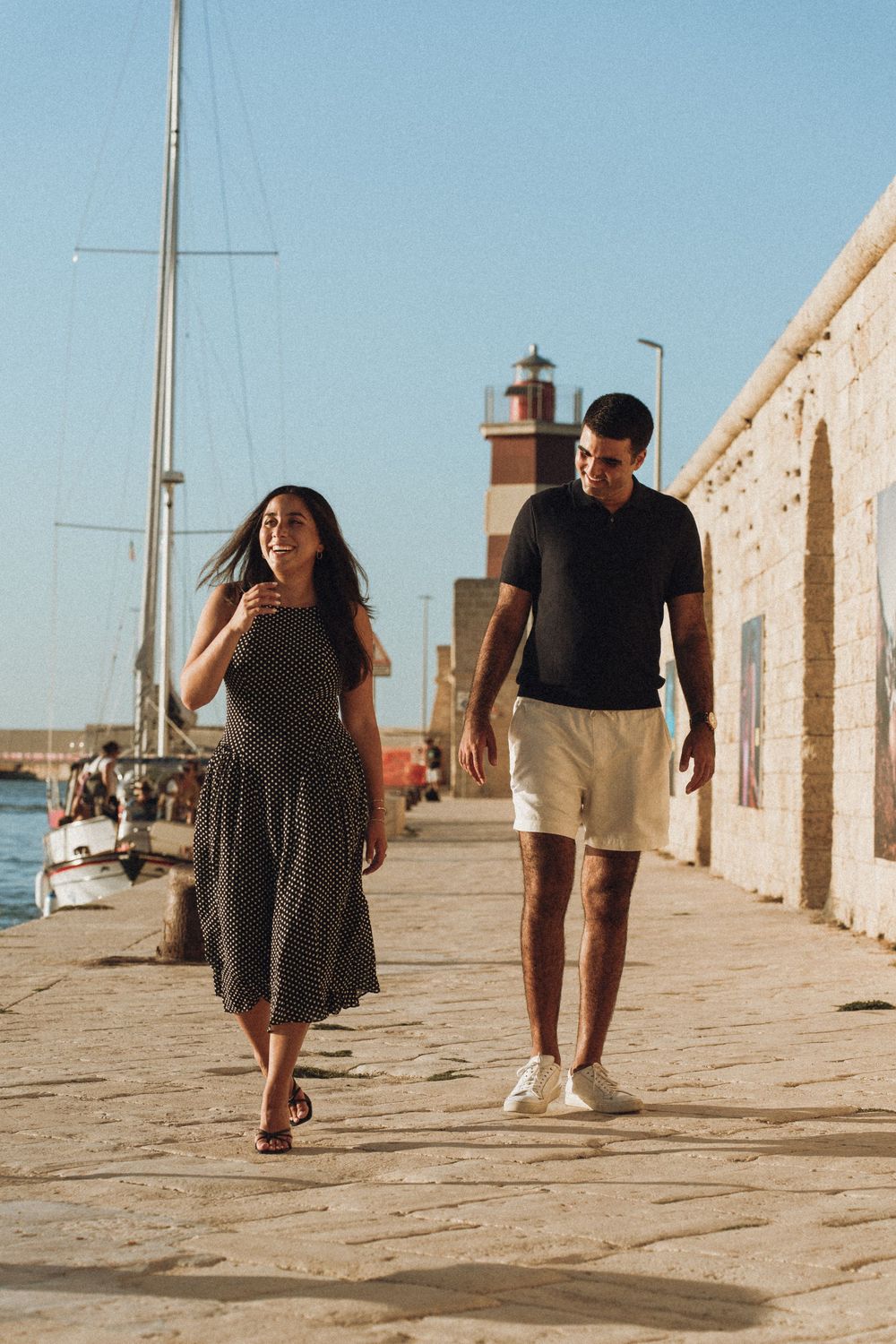 A sequence of photos showing two people walking along a sunlit seaside promenade with stone buildings and water in the background.