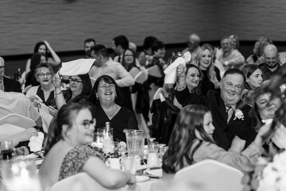 Black and white candid photo of wedding guests laughing at tables during a reception celebration.