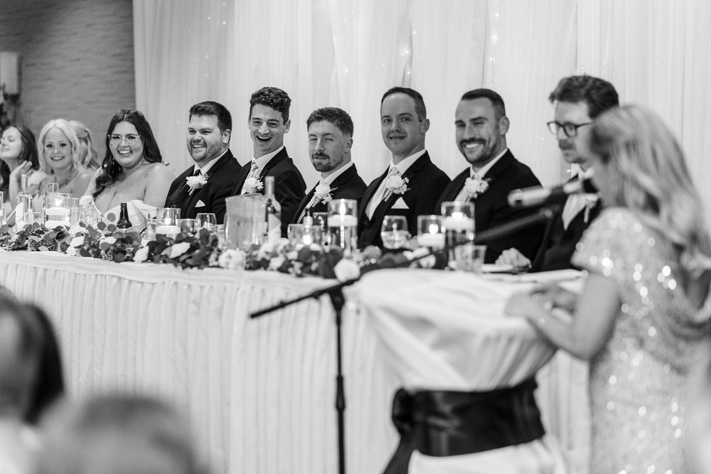 Black and white panoramic photo of wedding reception guests seated at long tables in an elegant banquet hall.