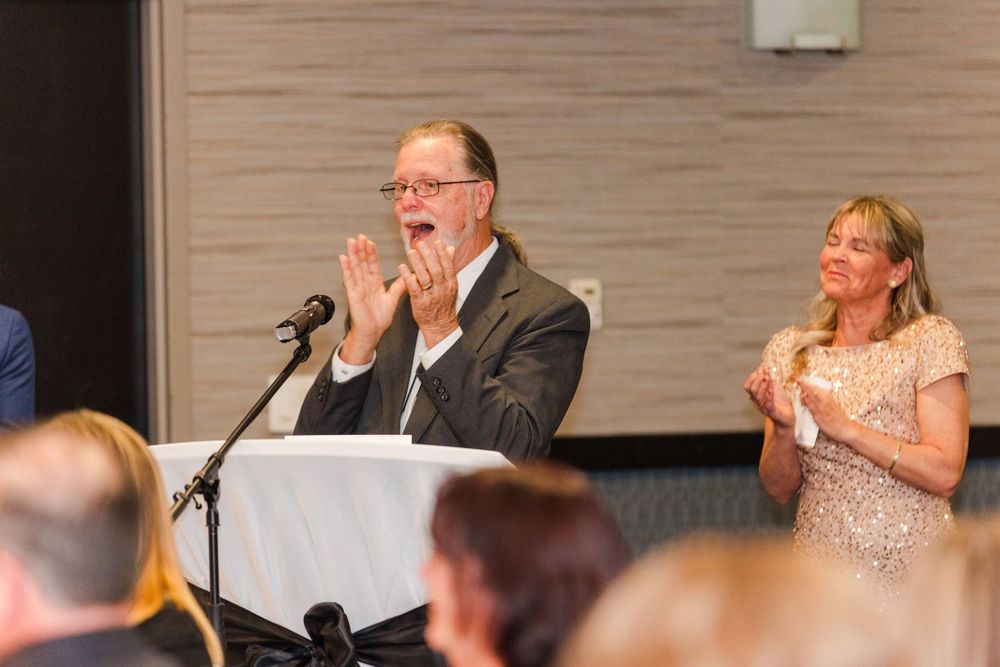 Wedding reception guests react with laughter and emotion during speeches in a banquet hall.