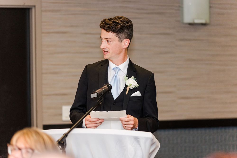 Person delivering a wedding speech at a reception podium with formal attire and decorations.