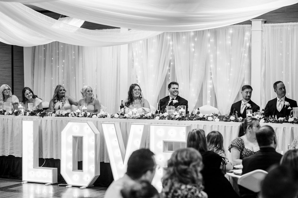 Wide angle black and white shot of wedding guests seated at decorated tables during an indoor reception.