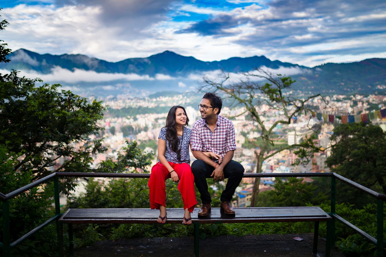 Couple sitting on bench overlooking a misty mountain cityscape.