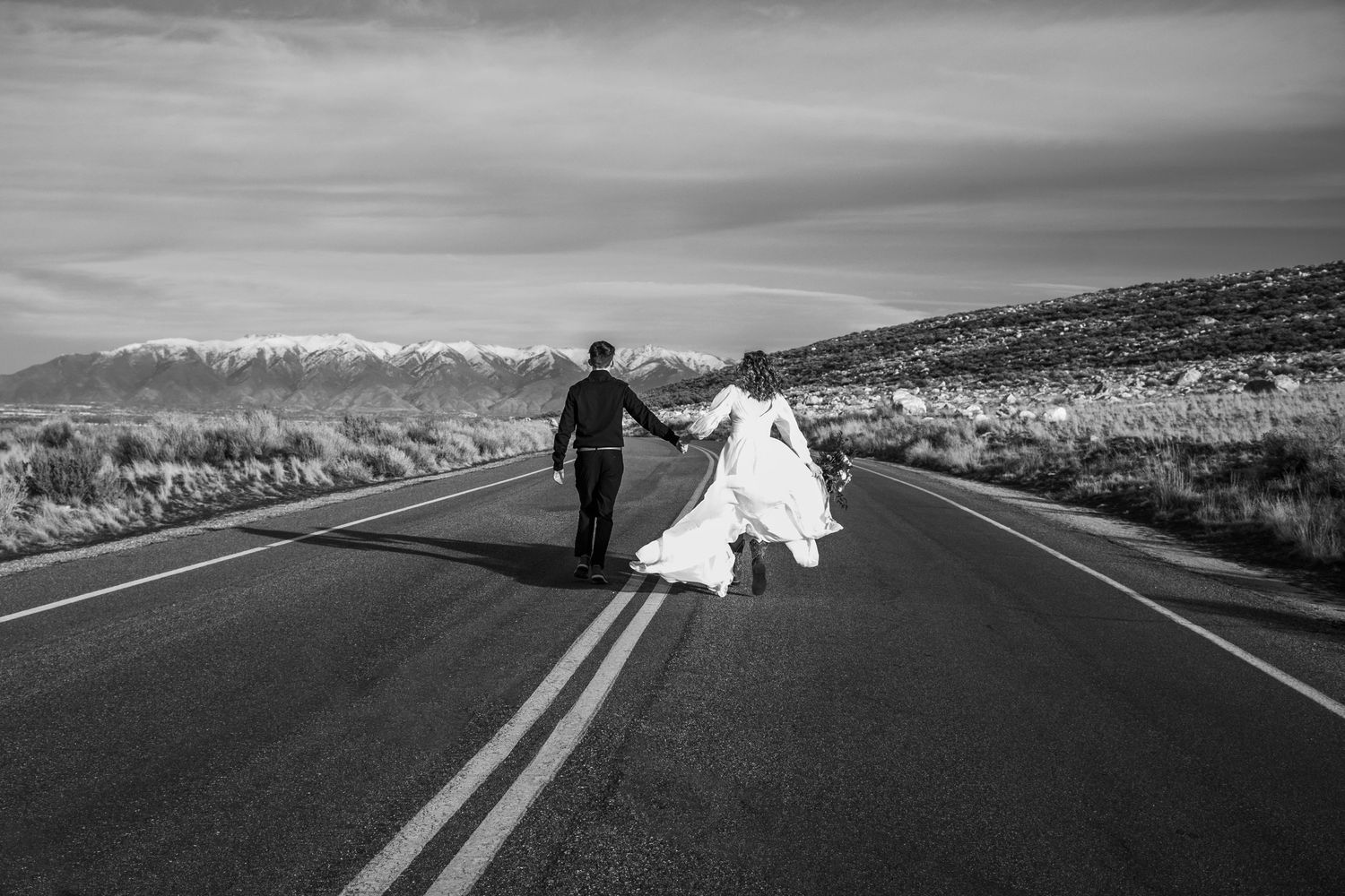 Bride and groom run cinematically away from camera in the middle of the road in Antelope Island.