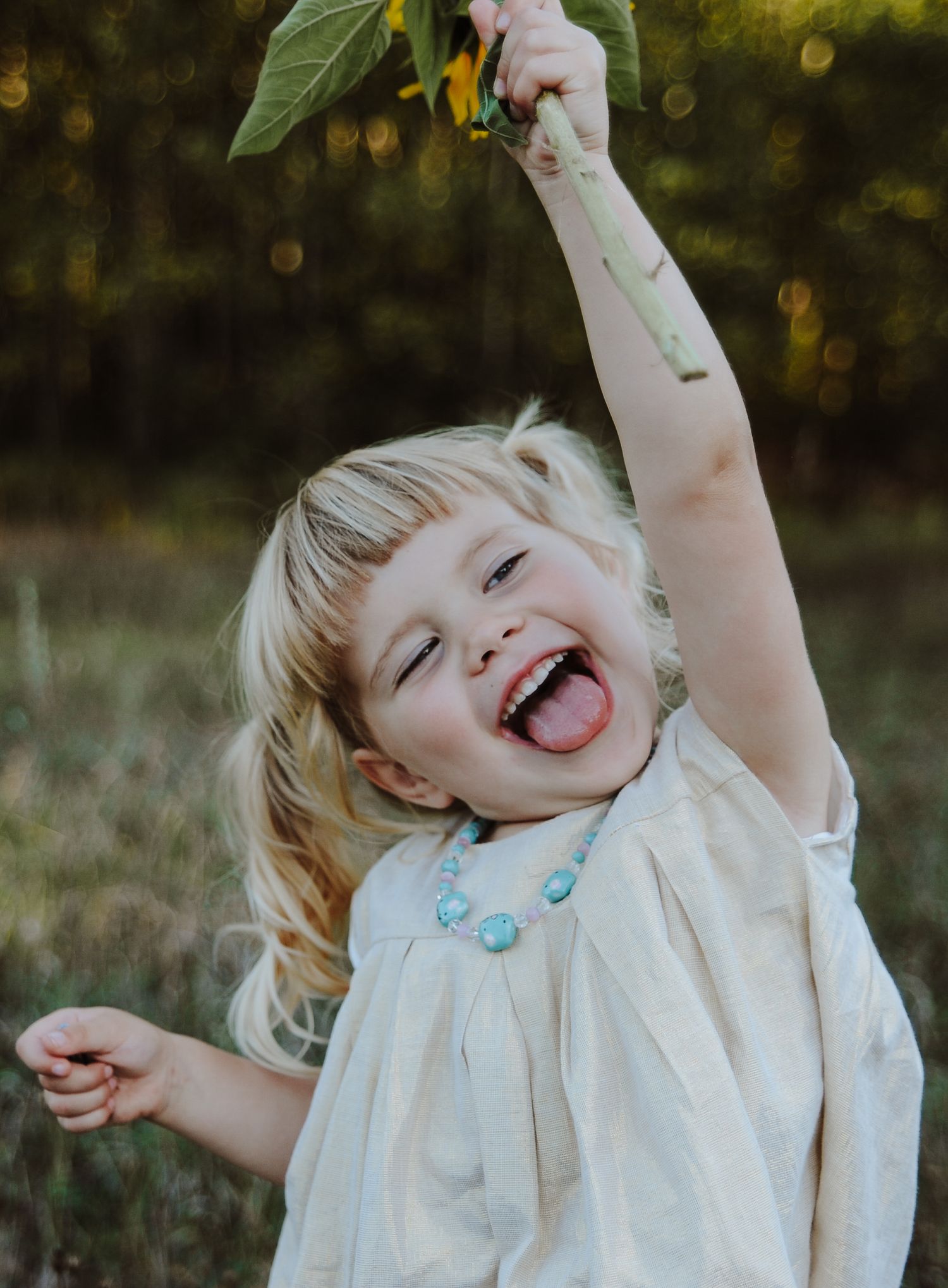 A young child in a white dress laughs joyfully while playing outdoors in a natural setting with golden bokeh lighting.