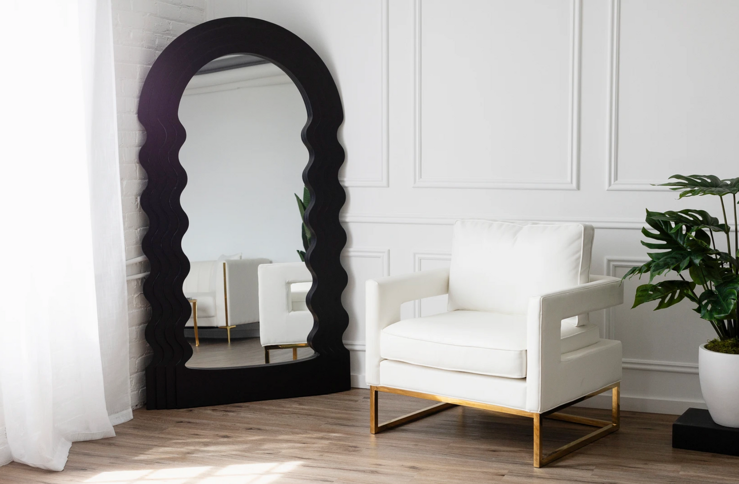 Minimalist white room interior with black arched mirror and modern accent chair.