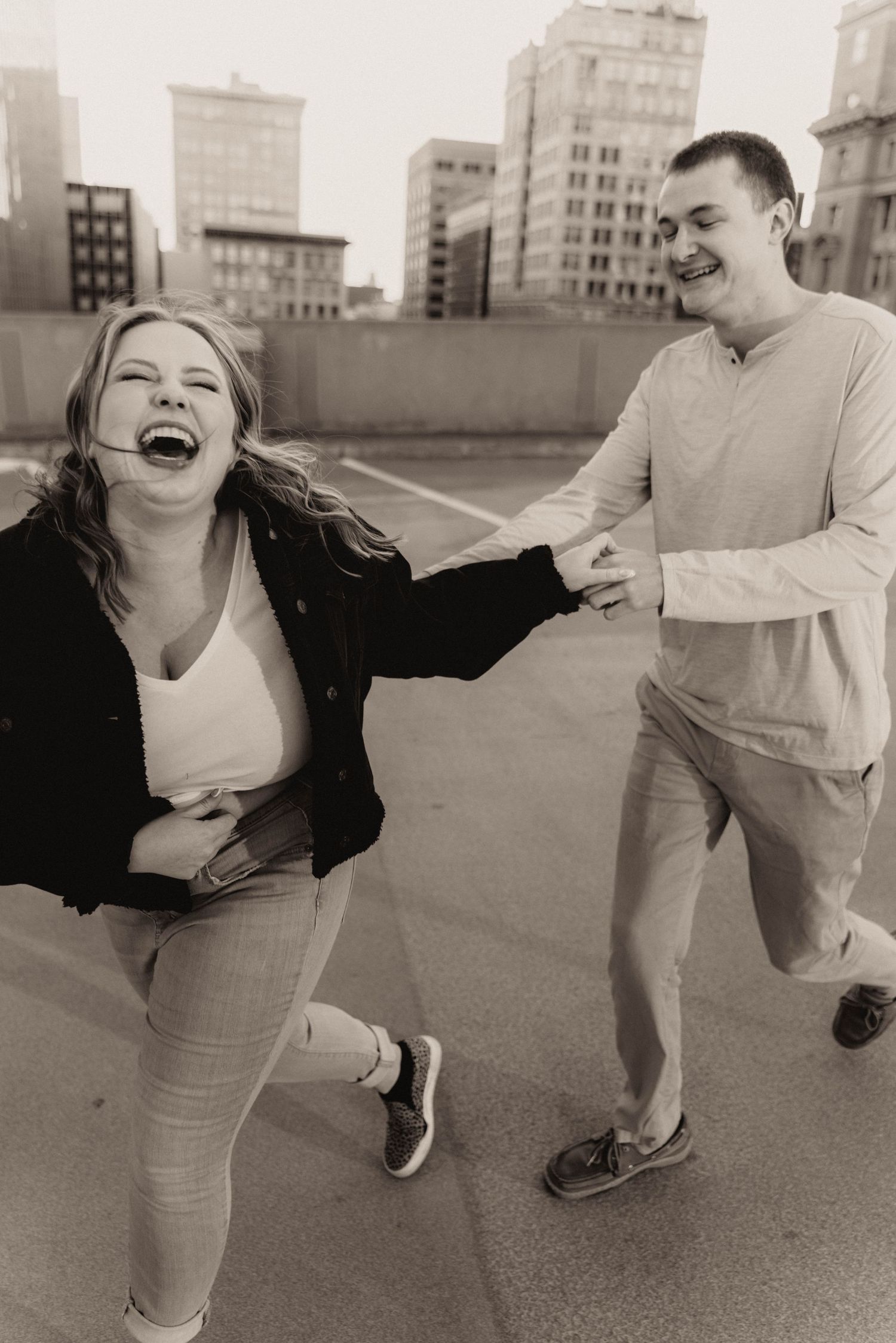 Joyful couple laughing and running on rooftop parking garage, black and white urban photo.
