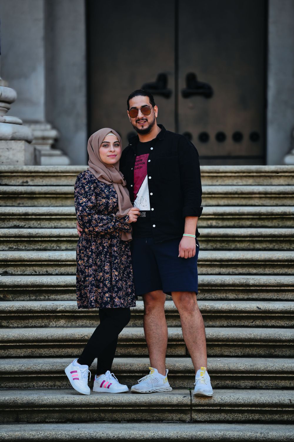 Stylish couple poses on grand stone steps outside historic building.